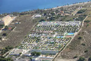 Luftaufnahme eines Campingplatzes am Meer mit vielen Stellplätzen, Palmen, Wegen und zwei blauen Pools.