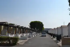 Reihe von Wohnwagen und kleinen Häusern entlang eines Wegs, mit Hecken, Laternen und geparktem Auto im Campingbereich.