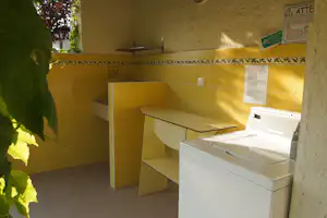 Waschraum im Campingbereich mit gelb gefliesten Wänden, Waschbecken, Ablage und Hinweisschild an der Wand.
