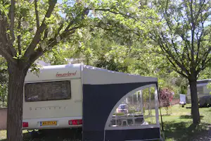 Wohnwagen mit Vorzelt auf einem Campingplatz, umgeben von hohen Bäumen und grünem Gras.