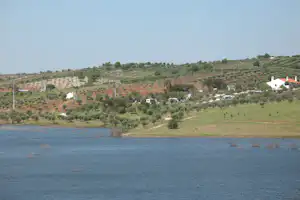 Campingplatz am See mit Olivenhainen, weißen Gebäuden mit roten Dächern und Wohnmobilen im Tal.