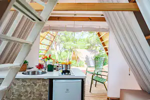 Küchenzeile mit Spüle und Elektrogrill im Zelt, daneben grüne Stühle auf der Holzterrasse, Blick in den Garten.