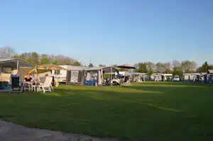 Campingplatz mit Wohnwagen und Zelten auf grünem Rasen, Sitzgruppen und Wäscheleinen im Hintergrund.