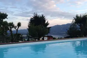 Campingpool mit blauem Wasser, Bäume und Blick auf den See und die Berge in der Ferne.