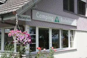 Rezeption am Campingplatz Ruderbaum mit Schild „Réception“, Blumen vor dem Gebäude und Fenstern unter dem Dach.