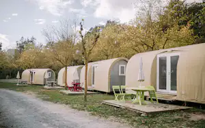 Reihe von Campingzelten mit Holzpodest und Sitzgelegenheiten am Stellplatz, umgeben von Bäumen und Rasen.