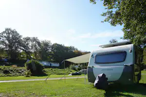 Wohnwagen auf einem Campingplatz im Grünen, daneben ein Vorzelt, Rasenfläche und Bäume am Rand.