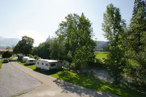 Wohnwagen auf einem Campingplatz entlang eines gepflasterten Wegs, umgeben von grünen Bäumen und Wiesen.