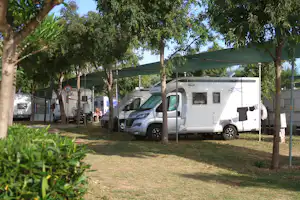 Wohnmobil unter einem Sonnensegel auf einem Campingplatz, daneben ein weiterer Camper und Bäume im Hintergrund.