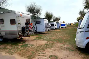 Wohnwagen auf einem Campingplatz, Fahrrad am Heckträger und weitere Camper auf dem Grasstellplatz zwischen Bäumen.
