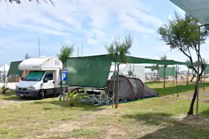 Wohnmobil mit grünem Vorzelt, davor Campingstühle und Zelt auf dem Stellplatz, Bäume und weitere Fahrzeuge im Hintergrund.