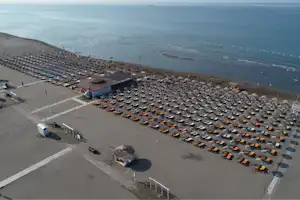 Strand-Campinganlage mit vielen Liegen und Sonnenschirmen am Sand, Blick aufs Meer und auf einen Strandabschnitt mit Booten.