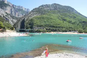 Bucht mit türkisfarbenem Wasser, Strand und Kajaks; im Hintergrund Berge und Felswände, eine Brücke über dem Fluss.