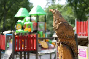 Nahaufnahme eines braunen Huhns auf dem Campingplatz, im Hintergrund ein Spielbereich mit bunten Schirmen und Absperrungen.