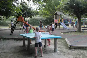 Spielplatz auf dem Campingplatz: Kinder rutschen und klettern an Rutsche und Klettergerüst im Schatten der Bäume.