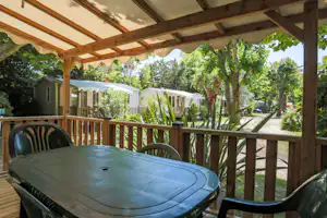 Terrasse mit Tisch und Stühlen, Blick auf Mobilheime und Bungalows im Grünen mit Bäumen und Wegen.