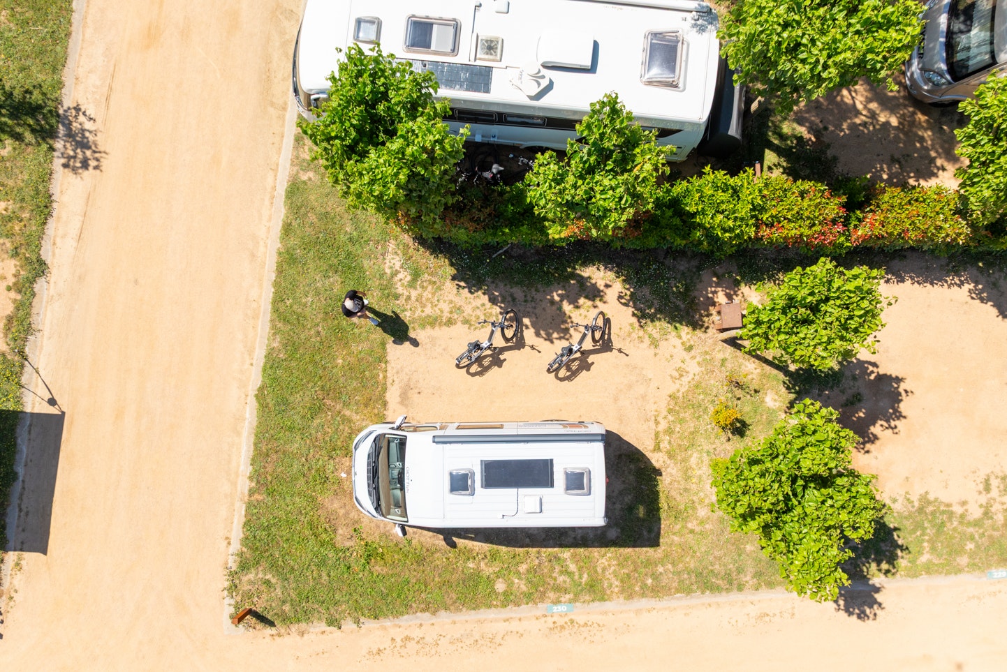 Zwei Wohnwagen auf einem Campingplatz mit Rasenfläche, Hecken und Wegen zwischen den Stellplätzen.