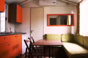 Wohnraum mit Küchenzeile, Esstisch und Sitzbank, große Tür und Fenster im Innenbereich eines Campingunterkunfts.