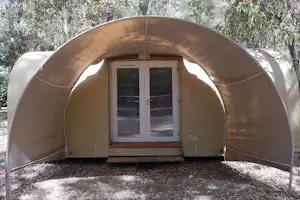 Zelt mit Fronttür und zwei Fenstern, im Hintergrund Bäume und Waldweg am Campingplatz.