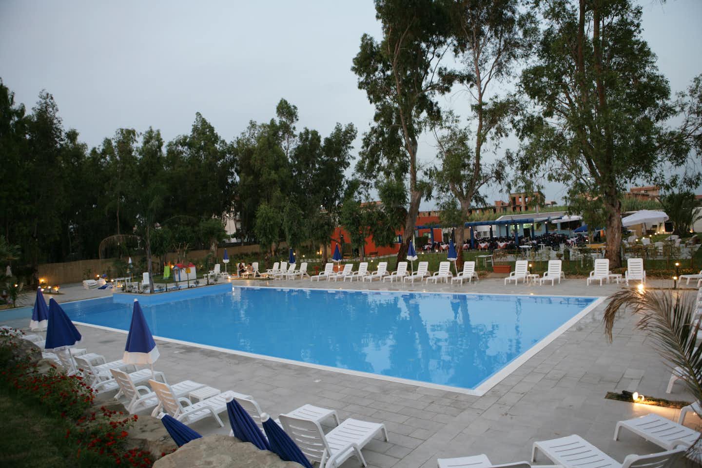 Camping Salicamp - Pool vom Campingplatz mit  Liegestühlen und Sonnenschirmen am Abend, Restaurant im Hintergrund
