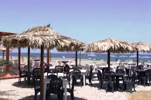 Camping Salicamp - Strand vom Campingplatz mit Restaurant und Essbereich draußen im Vordergrund, Liegestühle und Sonnenschirme am Meer im Hintergrund