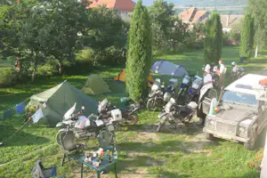 Campingplatz mit Zelten im Grünen, Motorräder am Stellplatz und Picknicktisch mit Getränken zwischen Bäumen.