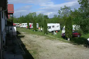 Campingplatz mit Wohnmobilen und Wohnwagen entlang eines Kieswegs, Hecken und Sitzgruppe vor einem Wohnwagen.