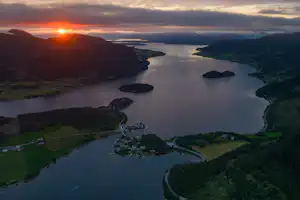 Weitblick auf einen Fluss im Tal mit mehreren Nebenarmen, grünen Hängen und Sonnenaufgang über der Landschaft.