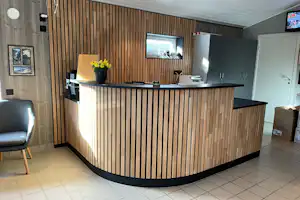 Rezeption mit Holztheke, Schreibtisch und Blumen auf der Theke, dahinter Schränke und ein Fernseher an der Wand.