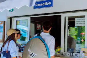 Rezeption eines Campingplatzes mit Schild „Reception“, zwei Personen vor dem Empfangstresen und Infomaterial an der Wand.