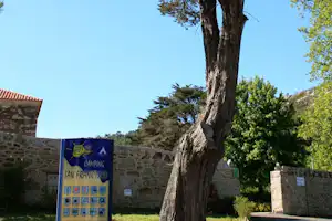 Camping-Eingangsschild „San Francisco“ vor einer Natursteinmauer, daneben Bäume und ein Weg im grünen Außenbereich.