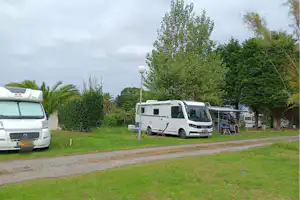 Wohnmobile auf einem Campingplatz, Kiesweg und grüner Rasen, Bäume und Hecken im Hintergrund.