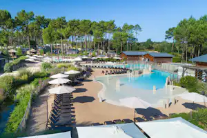 Großes Schwimmbecken mit Sonnenschirmen und Liegen, umgeben von Wegen, Bäumen und einem Holzgebäude am Campingplatz.