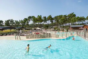 Schwimmbad auf dem Campingplatz mit Zaun, Liegen und mehreren Personen im Wasser vor Bäumen und Gebäuden.