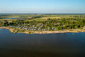 Luftaufnahme eines Campingplatzes am See mit Uferlinie, Stellplätzen und vielen Wohnwagen, umgeben von Wiesen und Bäumen.