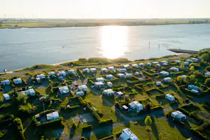 Luftaufnahme eines Campingplatzes am See mit vielen Stellplätzen, Wohnwagen und Zelten am Ufer.
