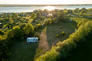 Ein Wohnwagen auf einem Campingplatz am Ufer, mit Graswegen, Bäumen und Blick auf den Fluss im Hintergrund.