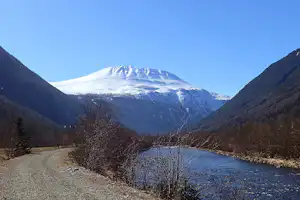 Blick ins Alpen-Tal mit schneebedecktem Berg zwischen bewaldeten Hängen und blauem Himmel.