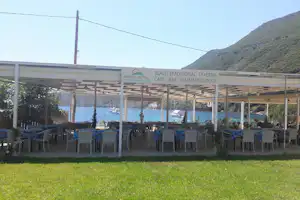 Terrasse mit vielen Stühlen und Tischen am Campingplatz, Blick auf das Meer und die Berge im Hintergrund.
