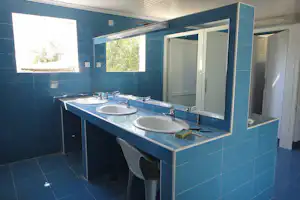 Blauer Sanitärraum mit drei Waschbecken, Spiegeln und Duschvorhangstange, daneben Türen und Fliesenboden.