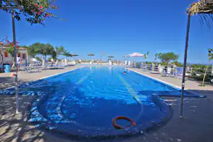 Blauer Swimmingpool mit Rundbecken, Liegen und Sonnenschirmen, Terrasse mit Pflanzen und Blick auf das Meer im Hintergrund.