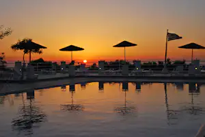 Pool auf der Terrasse mit Sonnenliegen, Sonnenschirmen und Blick auf die untergehende Sonne am Abendhimmel.