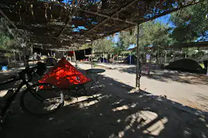 Zelt auf einem Campingplatz unter einem Schattendach, daneben Tisch und Stühle, im Hintergrund weitere Zelte und Bäume.