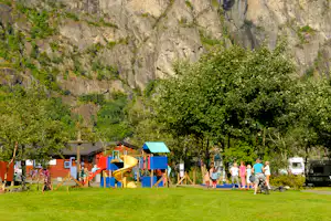 Spielplatz am Campingplatz mit Rutsche und Klettergerüst, im Hintergrund Bäume und eine steile Felswand.