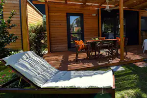Holzhaus mit Terrasse: Es gibt einen Esstisch, Stühle und eine Liege auf dem Rasen vor großen Fenstern.