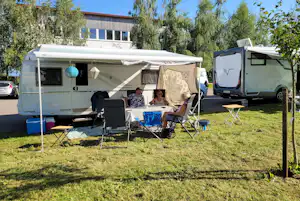 Wohnwagen mit Markise und Sitzgruppe auf dem Campingplatz, daneben ein Wohnmobil und ein Tisch mit Stühlen.