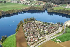 Luftaufnahme eines Campingplatzes am See mit vielen Stellplätzen, Wegen und Häusern am Ufer.