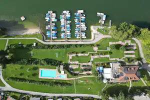 Luftaufnahme eines Campingplatzes mit mehreren Stellplätzen, Wohnmobilen und einem blauen Pool im grünen Gelände.