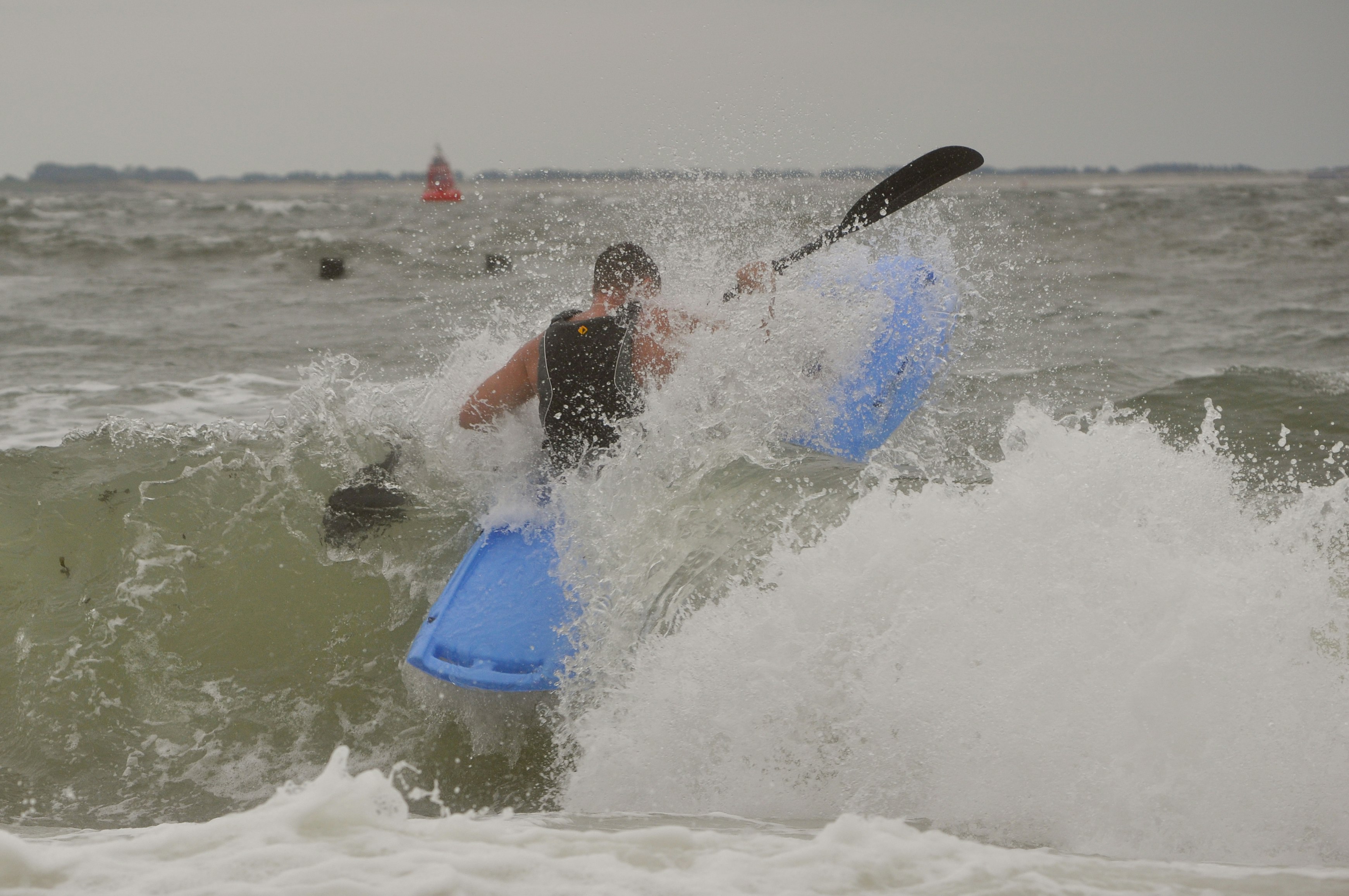 Zwei Surfer im Meer mit blauen Brettern, Wellen brechen am Strand, im Hintergrund weitere Personen im Wasser.