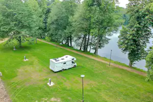 Wohnwagen auf einem Stellplatz im Grünen, mit Grasweg, Laternen und Bäumen am Ufer eines Flusses.